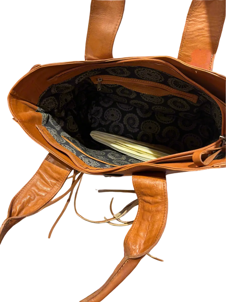 Brown leather tote bag with decorative handles on a white background