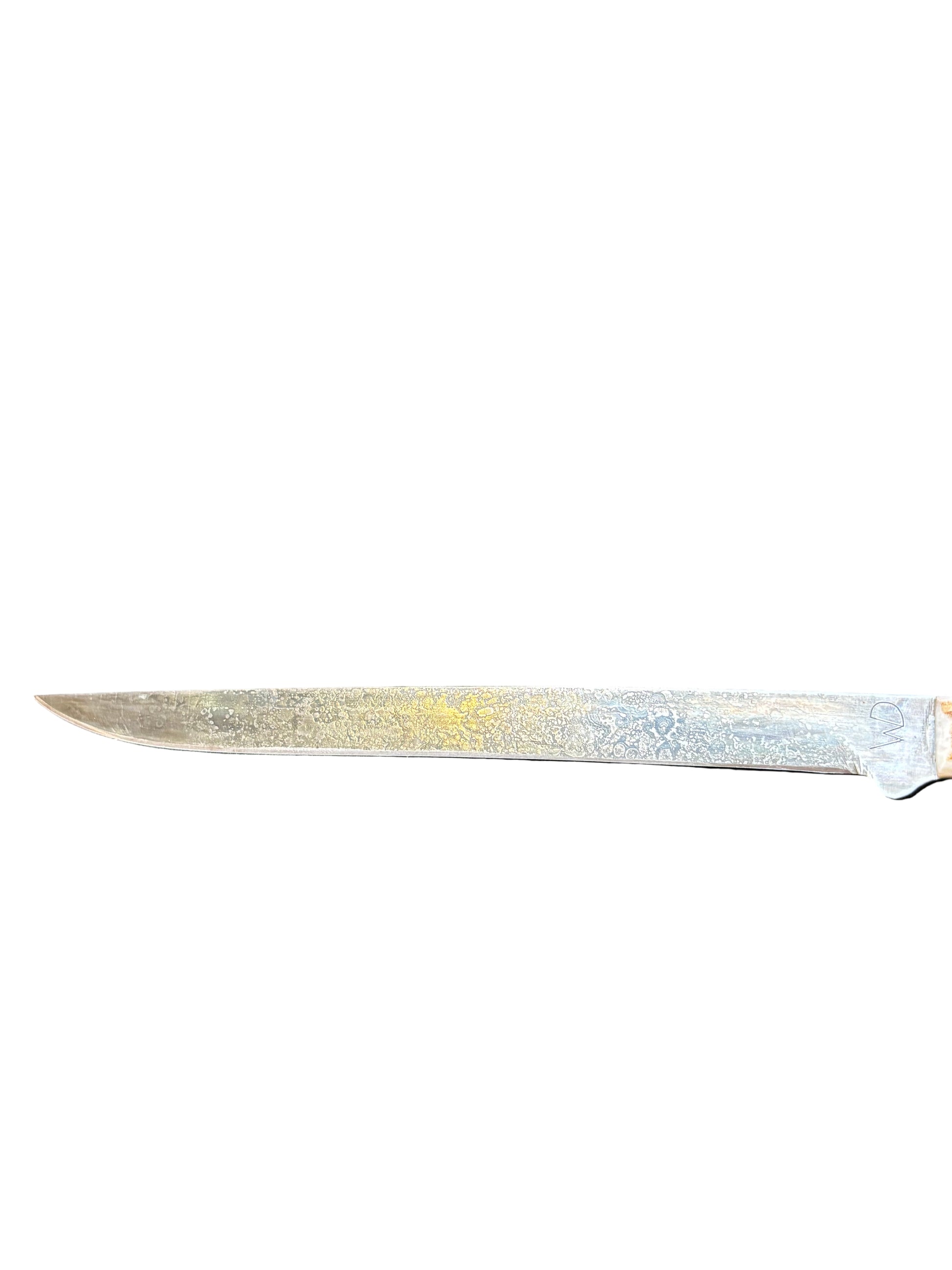 Long, thin metal blade on a textured black surface with wooden background