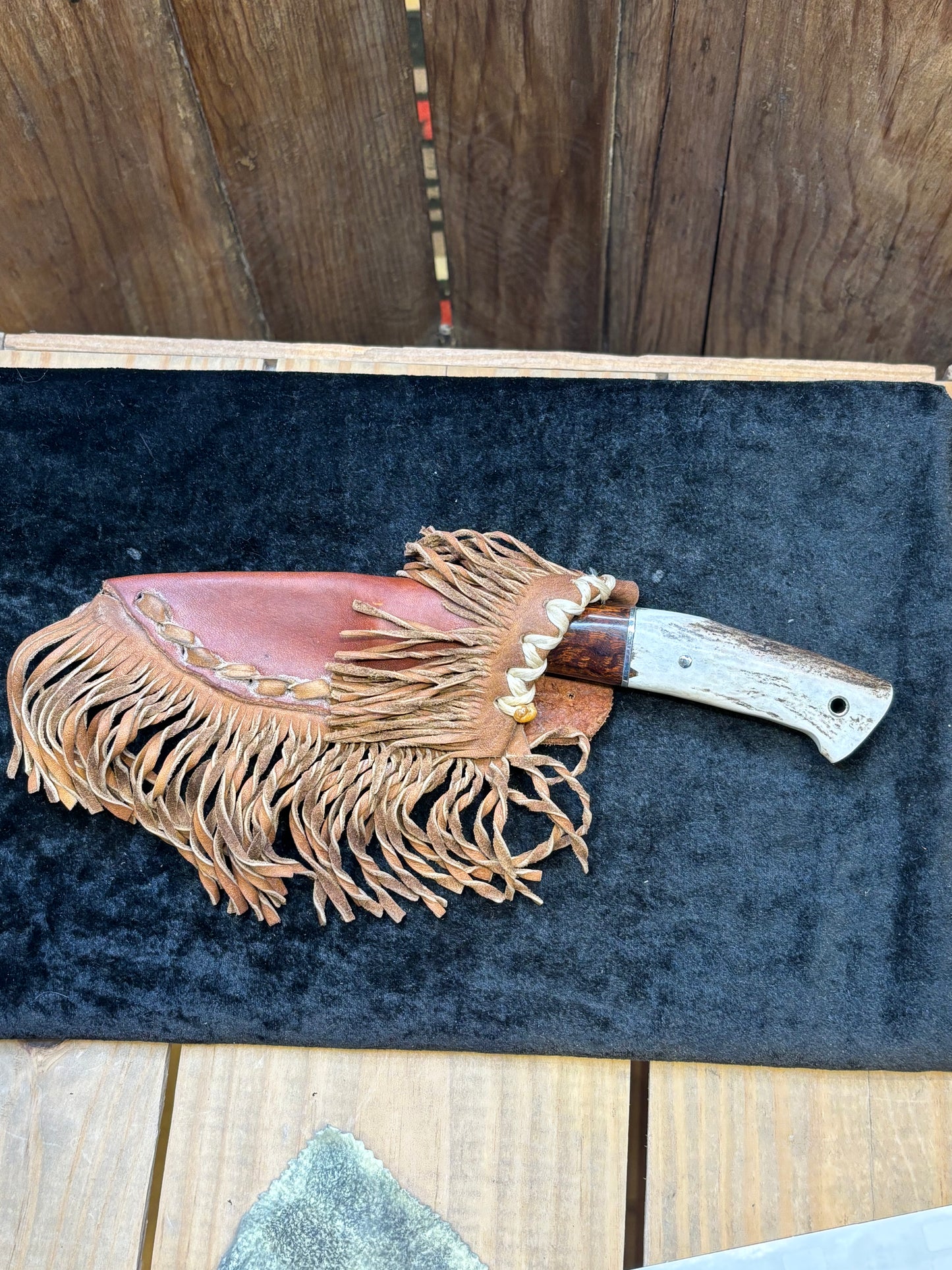 Decorative knife with fringes on a dark blue cushion against a wooden background