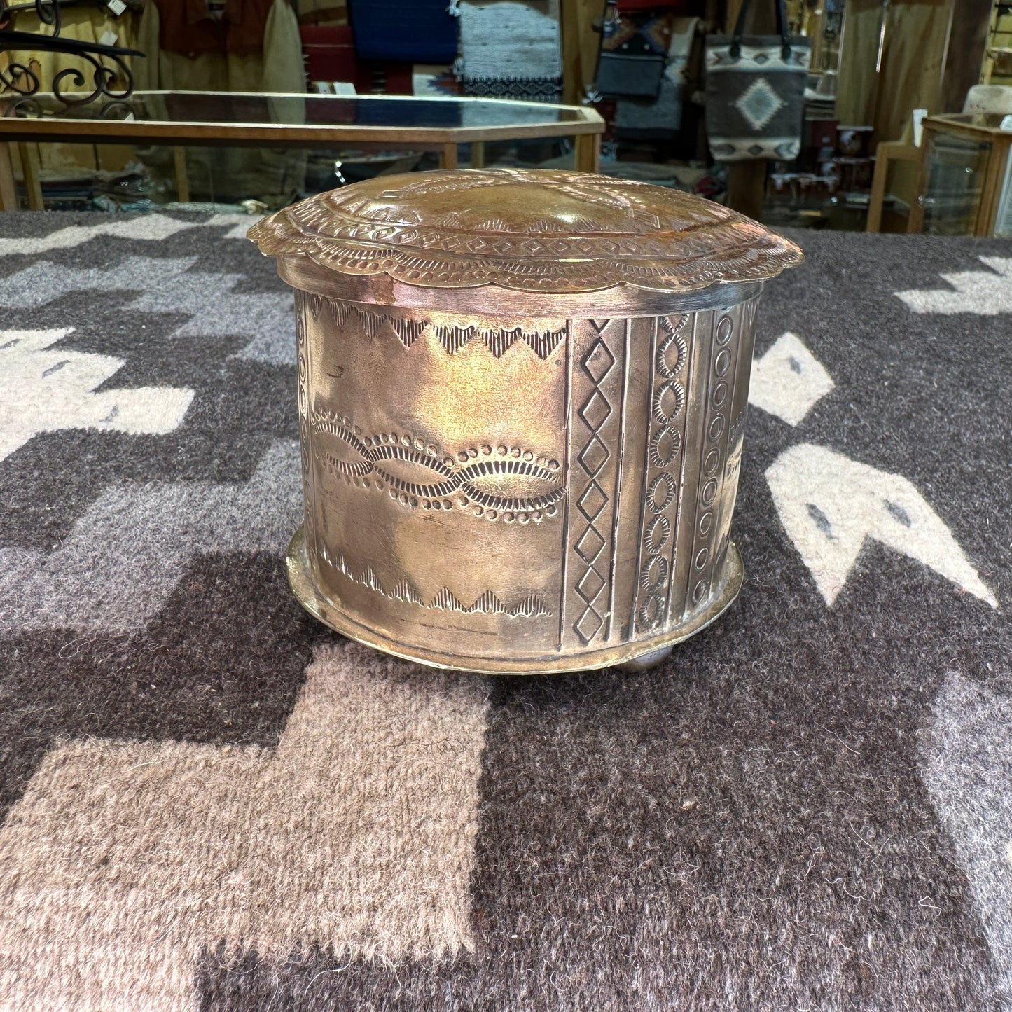 A silver box with intricate hand-tooled designs, displayed on a textured background.