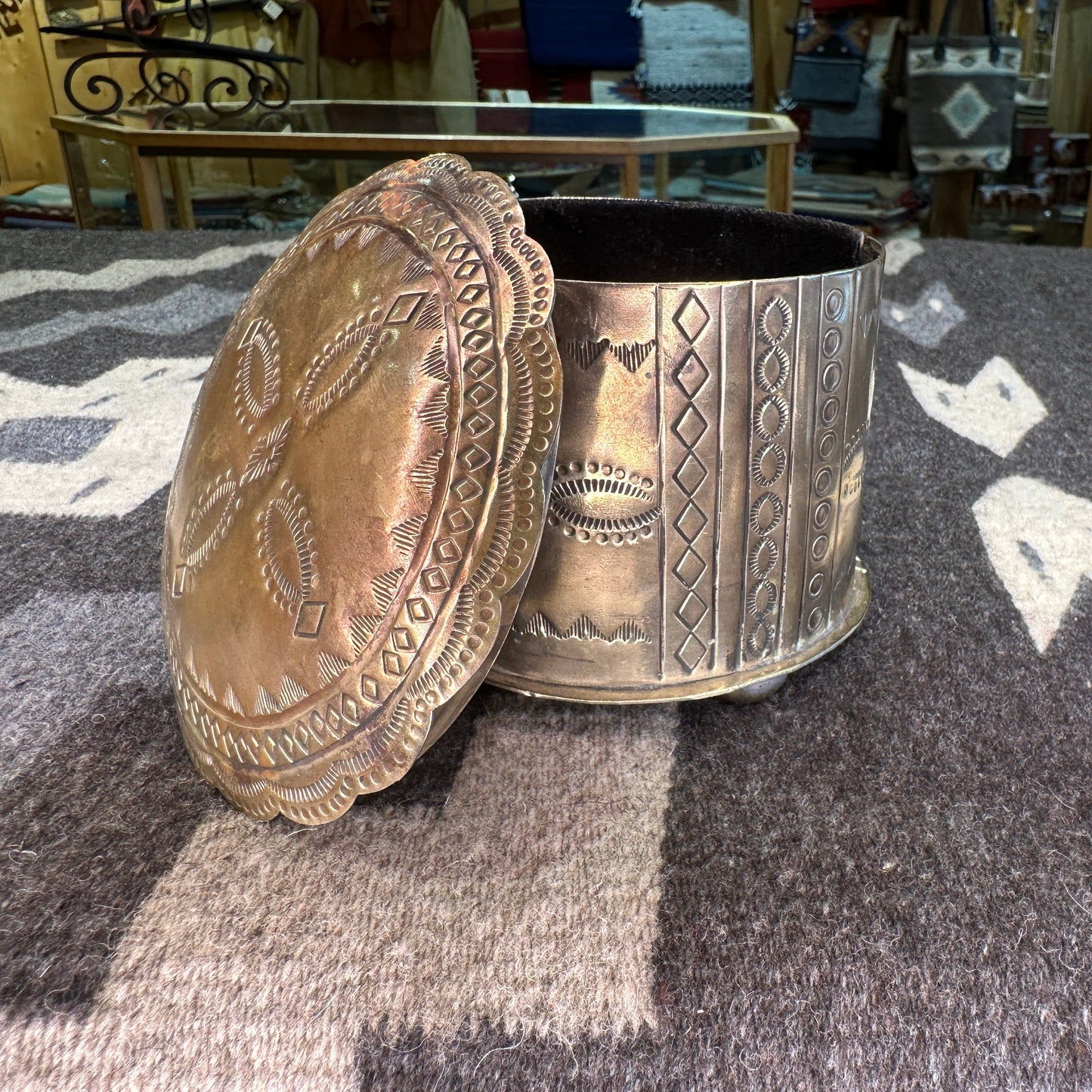 A silver box with intricate hand-tooled designs, displayed on a textured background.